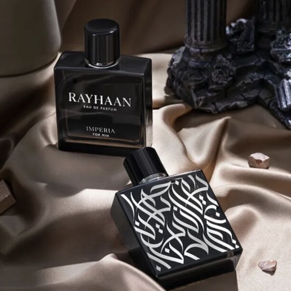 Two sleek black Rayhaan Imperia perfume bottles rest on silky fabric, surrounded by small stones and ruins, giving a luxurious and mysterious feel.