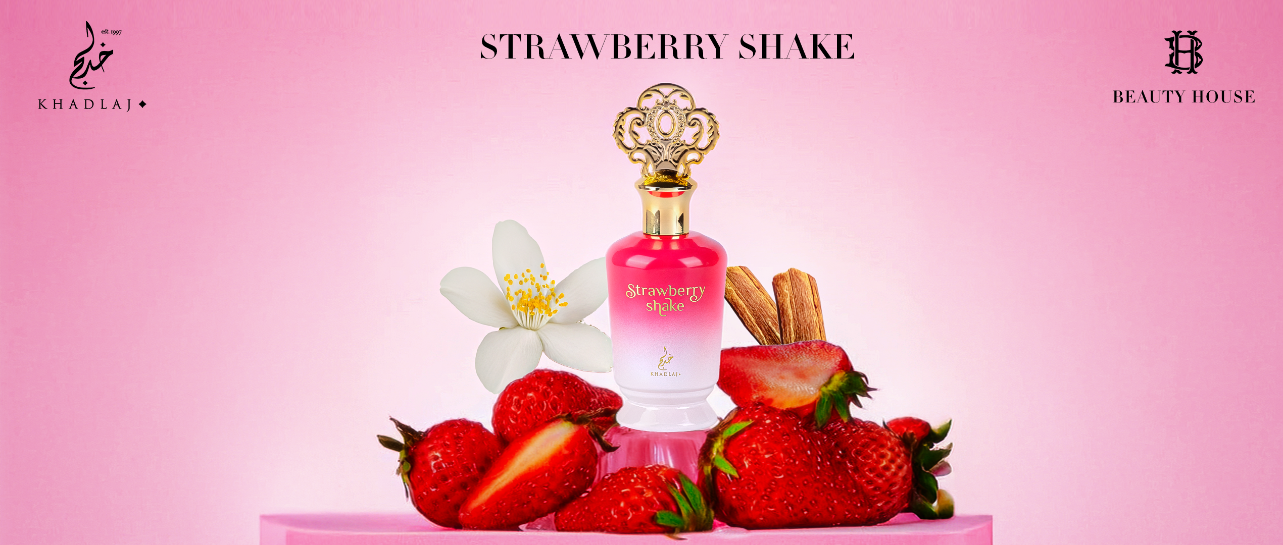 Here is a short, clear visual description for accessibility (blind-friendly), written as a single paragraph:
The image shows a bright pink background with a luxurious perfume bottle centered on a small pink platform. The bottle is pink-and-white with a gold ornate cap and the words “Strawberry Shake” printed on the front. Surrounding the bottle are fresh strawberries—some whole, some sliced—along with a white flower and sticks of cinnamon, suggesting the fragrance notes. The Khadlaj logo appears in the top